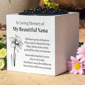 May include: A white memorial flower vase with a black floral insert on top. The vase has text that reads "In Loving Memory of My Beautiful Nana" and a poem with a daffodil illustration.