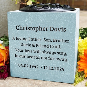May include: A light blue square memorial vase with a black flower holder on top. The vase has a personalised inscription that reads "Christopher Davis, A loving Father, Son, Brother, Uncle & Friend to all. Your love will always stay, In our hearts, not far away. 04.02.1942~12.12.2024".