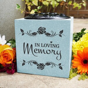 May include: A light blue square vase with a black plastic insert for flowers. The vase has a glitter finish and the words "In Loving Memory" are printed on the front.