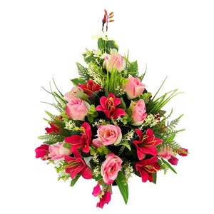 May include: A colourful floral arrangement with pink roses and deep red lilies, complemented by green foliage and small white flowers. The bouquet is carefully arranged, creating a visually appealing display.
