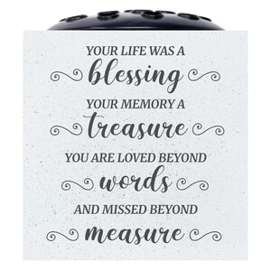May include: A white ceramic memorial vase with a black lid and a quote that reads: "Your life was a blessing, your memory a treasure, you are loved beyond words, and missed beyond measure."