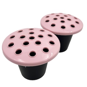 May include: Two pink flower frogs, each with multiple holes for arranging flowers. The top is light pink, and the base is black. The mushroom-shaped frogs are designed to hold flowers in place. Each frog is approximately 10 cm in diameter.