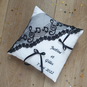 Coussin de mariage carré blanc avec prénoms et date de cérémonie brodés en noir. Dentelle sur tulle noir décor clé de sol et notes de musique en diagonale.