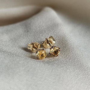 May include: A pair of gold stud earrings with small, round, yellow gemstones.