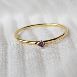 May include: A delicate gold band ring with a small purple gemstone in the centre.