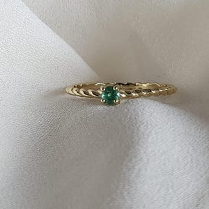 May include: A gold ring with a twisted band and a small green gemstone in the centre.