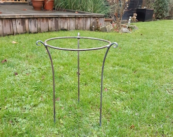 May include: A dark gray metal plant stand featuring a circular top ring supported by three slender, curved legs. The structure is constructed from thin metal rods, with each leg terminating in a decorative scroll detail at the top connection point.