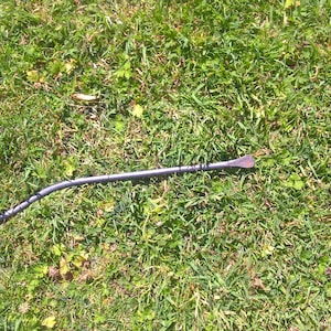 May include: A black metal crowbar with a curved handle lying on a green grassy surface.