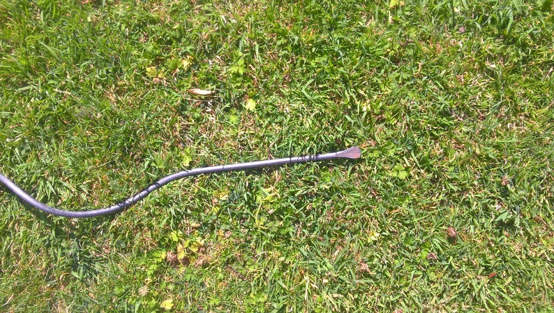 May include: A black metal crowbar with a curved handle lying on a green grassy surface.
