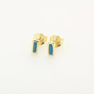 May include: A pair of gold stud earrings with a blue enamel rectangle in the center.