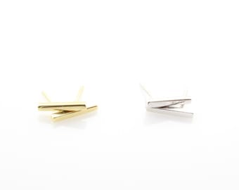 May include: A pair of minimalist earrings, one gold and one silver, each featuring two thin, straight bars that intersect at a slight angle.