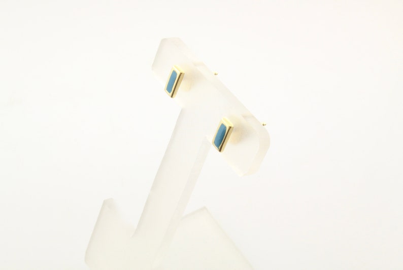 May include: A pair of gold stud earrings with a rectangular blue stone in the center.