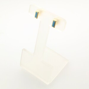 May include: A pair of gold stud earrings with a light blue rectangular stone in each earring.