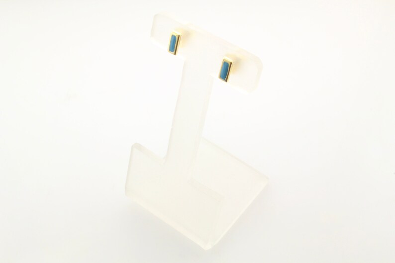 May include: A pair of gold stud earrings with a light blue rectangular stone in each earring.