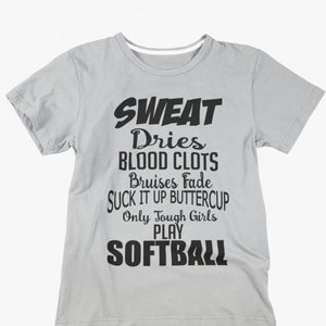 May include: A light gray t-shirt with black text. The text reads "SWEAT Dries BLOOD CLOTS Bruises Fade SUCK IT UP BUTTERCUP Only Tough Girls PLAY SOFTBALL". The shirt has short sleeves and a crew neck.