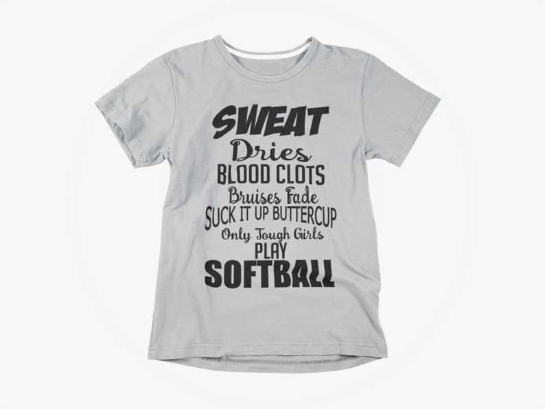 May include: A light gray t-shirt with black text. The text reads "SWEAT Dries BLOOD CLOTS Bruises Fade SUCK IT UP BUTTERCUP Only Tough Girls PLAY SOFTBALL". The shirt has short sleeves and a crew neck.