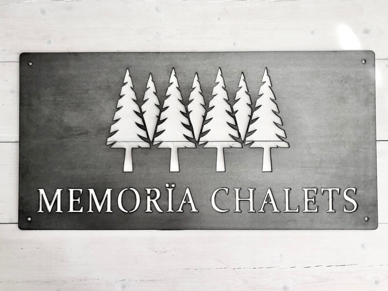 May include: A metal sign with a silhouette of five pine trees and the text "MEMOR&Auml; CHALETS".