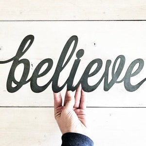 May include: A black metal sign with the word "believe" written in a cursive font.
