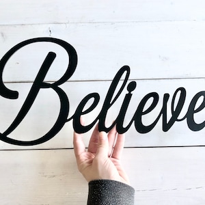 May include: Black metal wall decor with the word "Believe" in a cursive font.