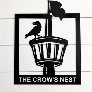 May include: Black metal sign with a crow perched on a tower with a flag. The sign reads "The Crow's Nest".