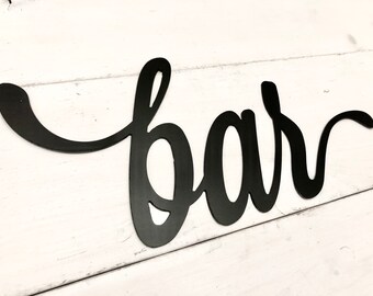 May include: Black metal sign with the word "bar" written in a cursive font.
