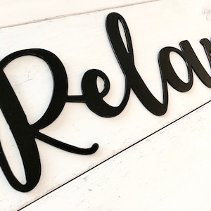 May include: Black metal wall decor with the word "Relax" in a cursive font.