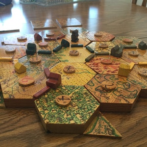 May include: A wooden board game with hexagonal tiles, each with a different design and number. There are small wooden pieces in various colors and shapes on the board.