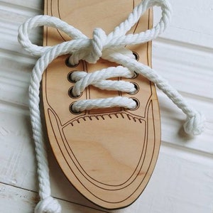 May include: Wooden shoe with white laces for tying practice. The shoe is made of light wood and has a simple design.