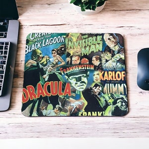 Puede incluir: Una alfombrilla de ratón con un collage de carteles de películas de terror clásicas. Los carteles incluyen "La Criatura de la Laguna Negra", "El Hombre Invisible", "Frankenstein", "Drácula" y "La Momia".