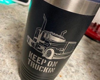 May include: A black stainless steel tumbler with a silver lid. The tumbler has a white graphic of a semi-truck with the text "KEEP ON TRUCKIN'" underneath.