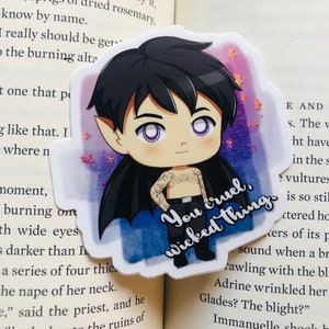 Peut inclure: Un autocollant représentant un vampire de dessin animé avec des yeux violets et une cape noire. Le vampire porte une chemise et un pantalon noirs et a des tatouages sur les bras. L'autocollant a un fond pailleté et le texte "You cruel, wicked thing" est écrit en blanc.