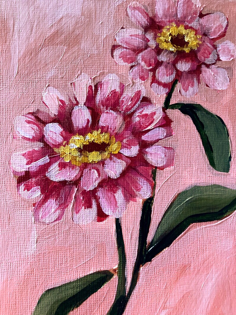 May include: An original oil painting of two pink zinnias with yellow centers and green leaves against a pink background. The flowers have multiple layers of petals, and the brushstrokes are visible, giving the painting a textured appearance.