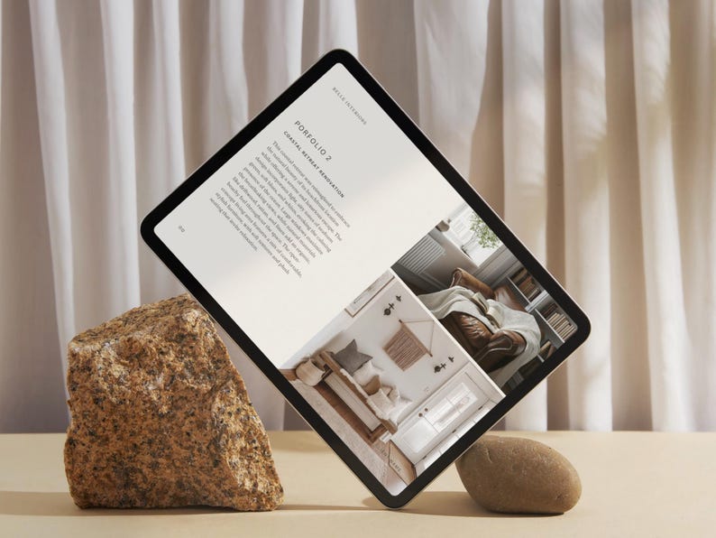 May include: A digital tablet displaying a portfolio of interior design work. The tablet is propped up on a rock and shows a photo of a living room with a sofa, a bench, and a rug. The text on the tablet reads "Portfolio 2:  Coastal Retreat Renovation".