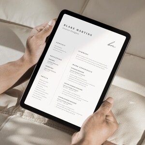 May include: A black tablet displaying a resume for Blake Martins, Interior Designer. The resume includes sections for contact information, education, skills, summary, and work experience. The tablet is held by a person.