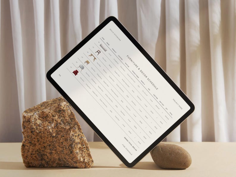 Pode incluir: Um tablet branco com moldura preta est&aacute; apoiado em uma rocha. A tela exibe uma programa&ccedil;&atilde;o de m&oacute;veis e decora&ccedil;&atilde;o com uma lista de itens, quantidades e pre&ccedil;os. O texto "Furniture & Decor Schedule" &eacute; vis&iacute;vel na parte superior da tela.