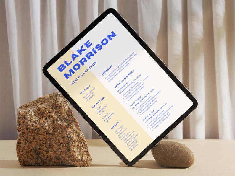 May include: A digital tablet displaying a CV for Blake Morrison, an Industrial Designer. The CV includes sections for contact information, education, work experience, skills, and a summary. The tablet is propped up on two rocks.