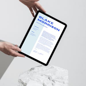 May include: A digital tablet displaying a CV for Blake Morrison, an Industrial Designer. The CV is on a white background with blue text. The tablet is held in the air by two hands.