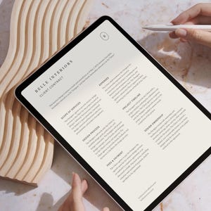 Può includere: Primo piano di un tablet che mostra un contratto cliente per Belle Interiors. Il contratto descrive la portata dei servizi, il processo di progettazione, la tempistica del progetto, le tariffe e il pagamento, e la proprietà del design.