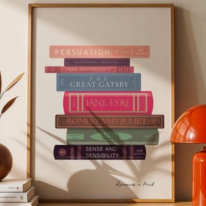 Könnte beinhalten: Ein gerahmter Druck mit einer Ansammlung klassischer Buchtitel wie "Persuasion" und "The Great Gatsby." Die Bücher sind in verschiedenen Farben gehalten, mit dem Text "Romance in Print" unten. Eine rote Lampe und eine Vase mit getrockneten Pflanzen stehen auf einem Holzschrank.