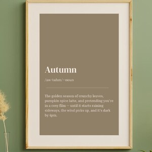 May include: A framed print defining "Autumn" in white text on a brown background, with a wooden frame. The print is displayed on a green wall above a wooden cabinet, with decorative items and a plant.