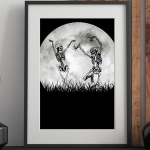 Op de afbeelding: Ingelijste kunstdruk met twee dansende skeletten voor een volle maan. De zwart-wit illustratie toont de skeletten op een grasveld, met de maan op de achtergrond. Het kunstwerk is ingelijst in een zwart frame.