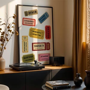 May include: A framed poster featuring vintage-style ticket designs with various place names, including "Byker" and "Haymarket Bus Station." A record player sits on a black cabinet, with a vase of dried branches to the left. The room has a warm, inviting atmosphere.