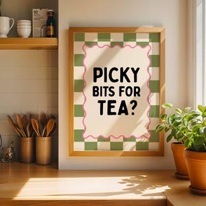May include: A framed wall art print featuring a green and white checkered background with a cream-colored central rectangle outlined in a pink wavy border. The text "PICKY BITS FOR TEA?" is printed in bold black sans-serif capital letters.