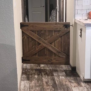 May include: A rustic wooden gate with a diagonal cross design, painted in a dark brown stain. The gate is mounted on a wall and has a metal latch.