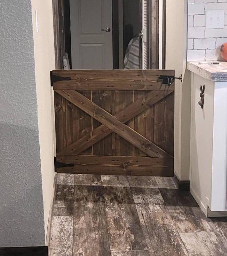 May include: A rustic wooden gate with a diagonal cross design, painted in a dark brown stain. The gate is mounted on a wall and has a metal latch.