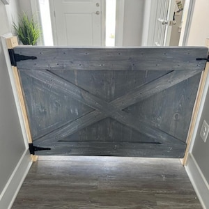 May include: A gray wooden gate with a criss-cross design and black hinges. The gate is installed in a doorway.