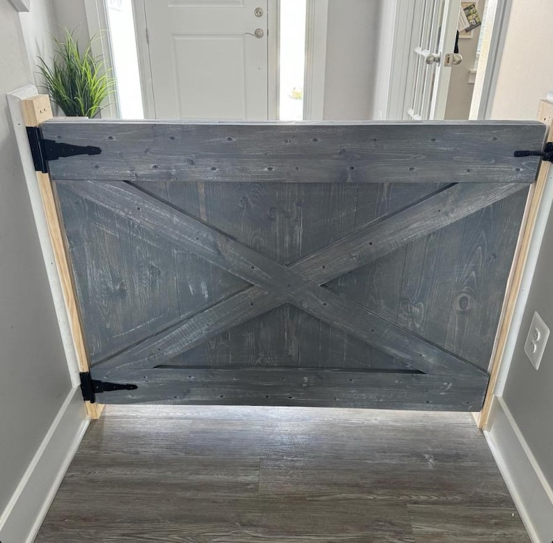 May include: A gray wooden gate with a criss-cross design and black hinges. The gate is installed in a doorway.