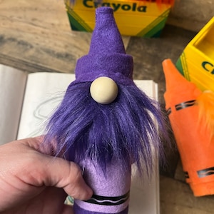 May include: Purple crayon gnome with a purple hat and a white wooden nose. The gnome is made from a purple crayon and has a fuzzy purple beard.