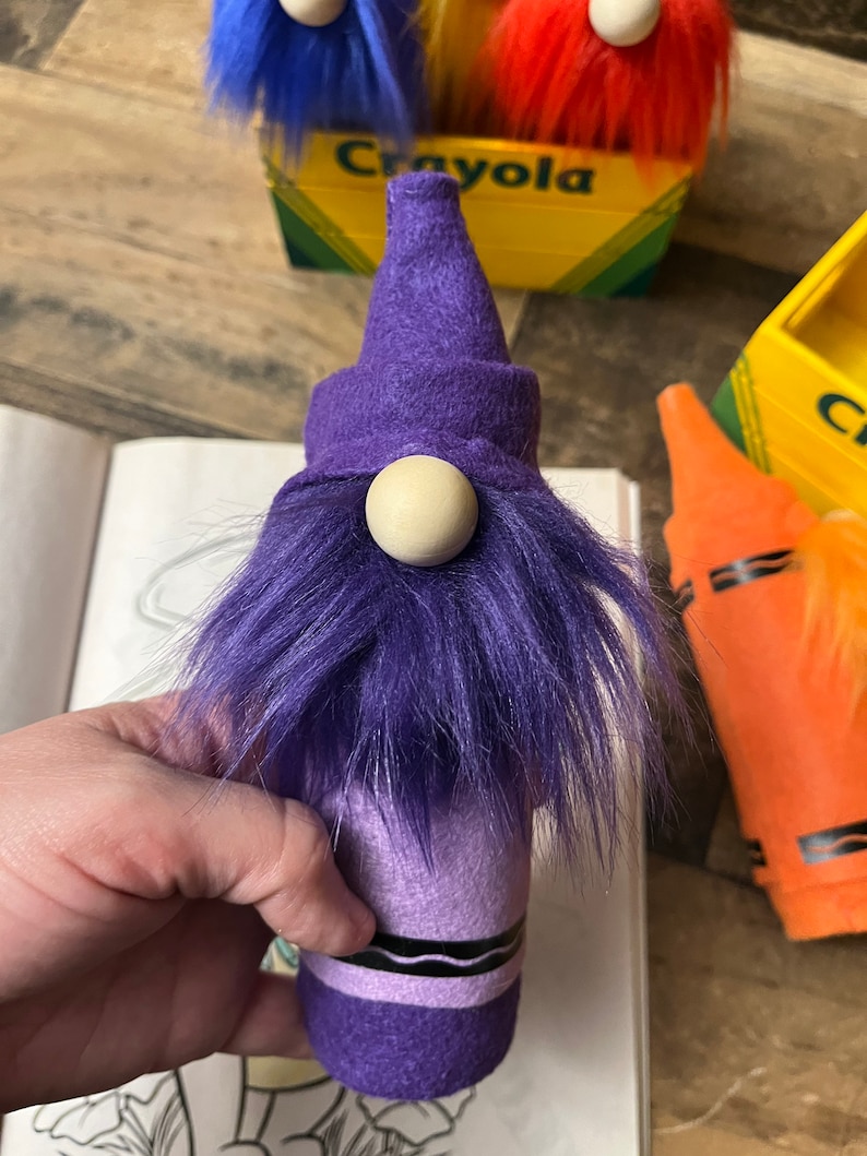 May include: Purple crayon gnome with a purple hat and a white wooden nose. The gnome is made from a purple crayon and has a fuzzy purple beard.