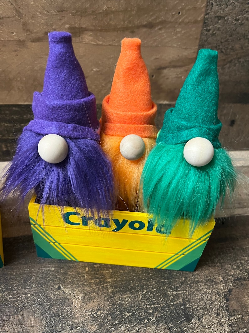 May include: Three gnomes with purple, orange, and green felt hats and fuzzy white beards sitting in a yellow wooden box with the word "Crayola" printed on the front.